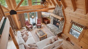 Interior acogedor de una cabaña con chimenea de piedra, vigas de madera, un sofá y una mesa de comedor.