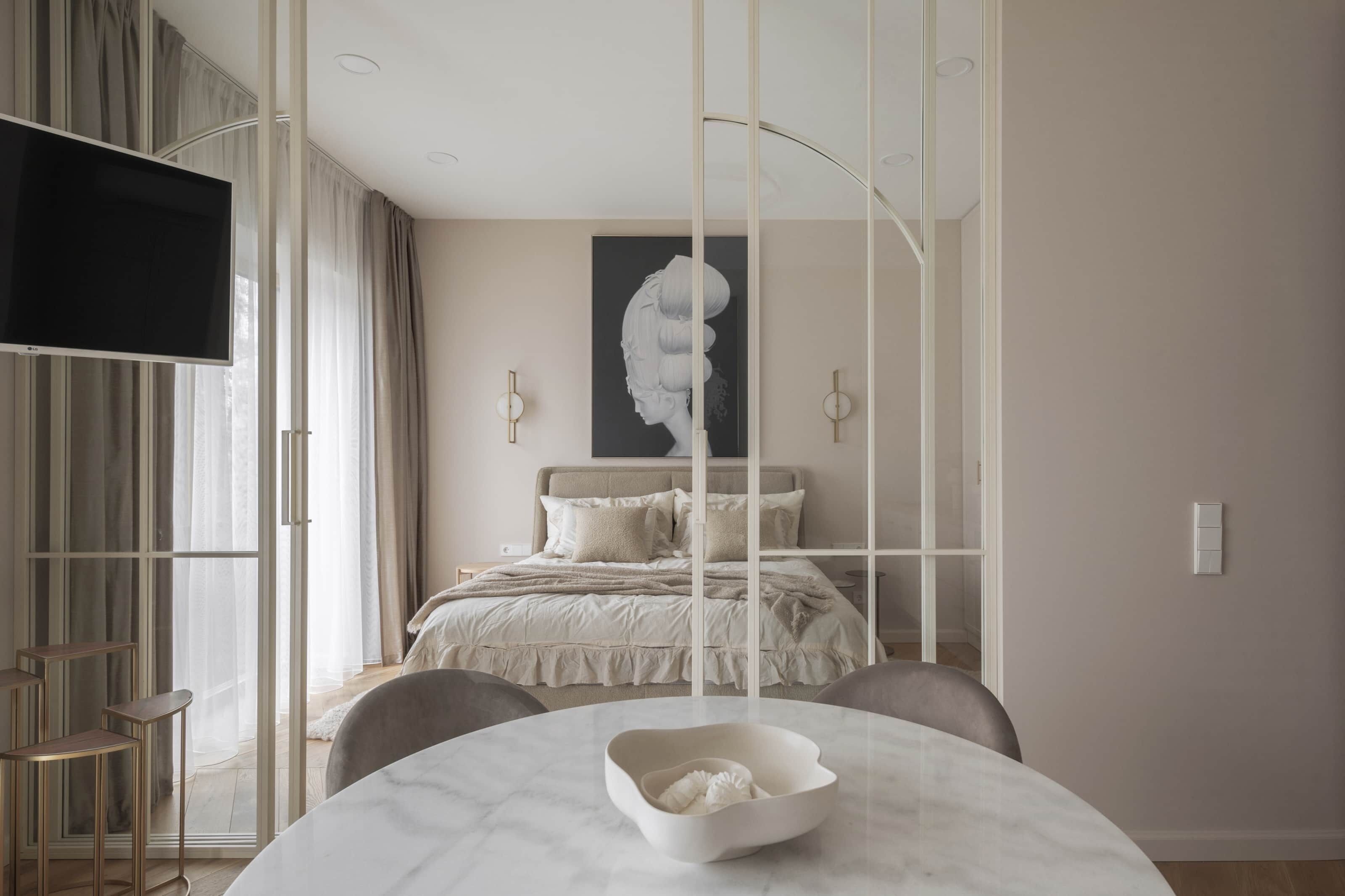 A modern bedroom with a bed, a TV, a dining table, and a large window with curtains.