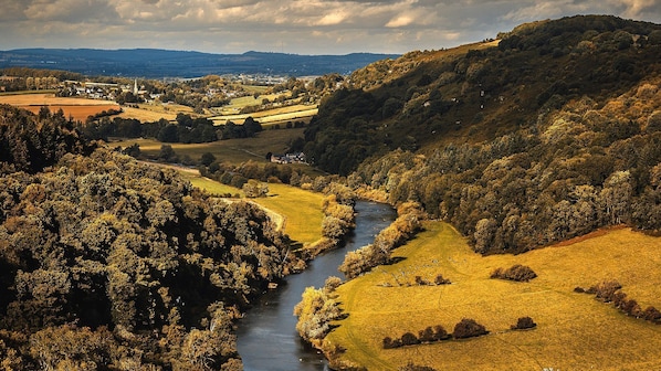 Un río serpentea por un valle con campos y un pueblo lejano.
