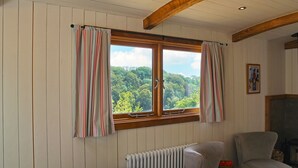 A room with a large window, wooden beams, a radiator, and a chair.