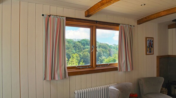 Una habitación con un ventanal grande, vigas de madera, un radiador y una silla.