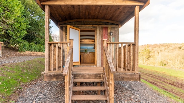 A wooden cabin with a porch, steps leading to a door, and a view of the surrounding landscape.