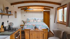 A compact room with a bed, a small table with breakfast items, a kitchenette with a stove, and a window with curtains.