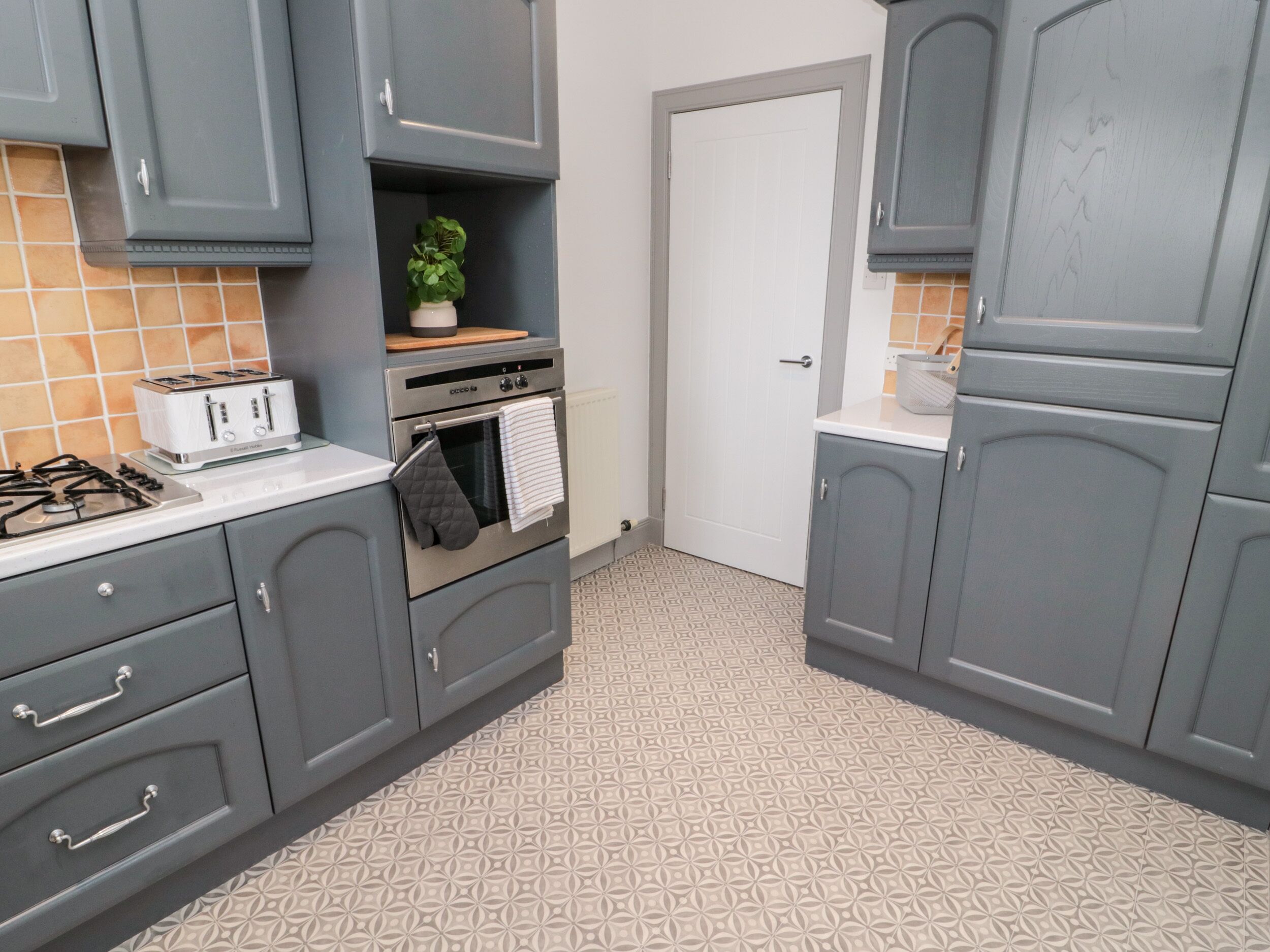 A kitchen with grey cabinets, a toaster, an oven, and a tiled backsplash.