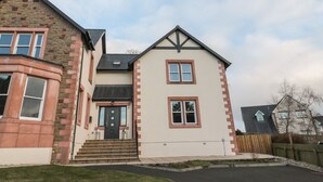 Une maison à deux étages avec une façade en pierre, une porte noire et un petit jardin devant.