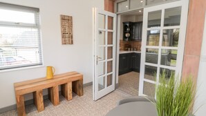 Une cuisine moderne avec des meubles de couleur sombre et un pare-feu en carreaux, un banc en bois avec une tasse jaune, et une grande porte-fenêtre coulissante donnant sur un patio.