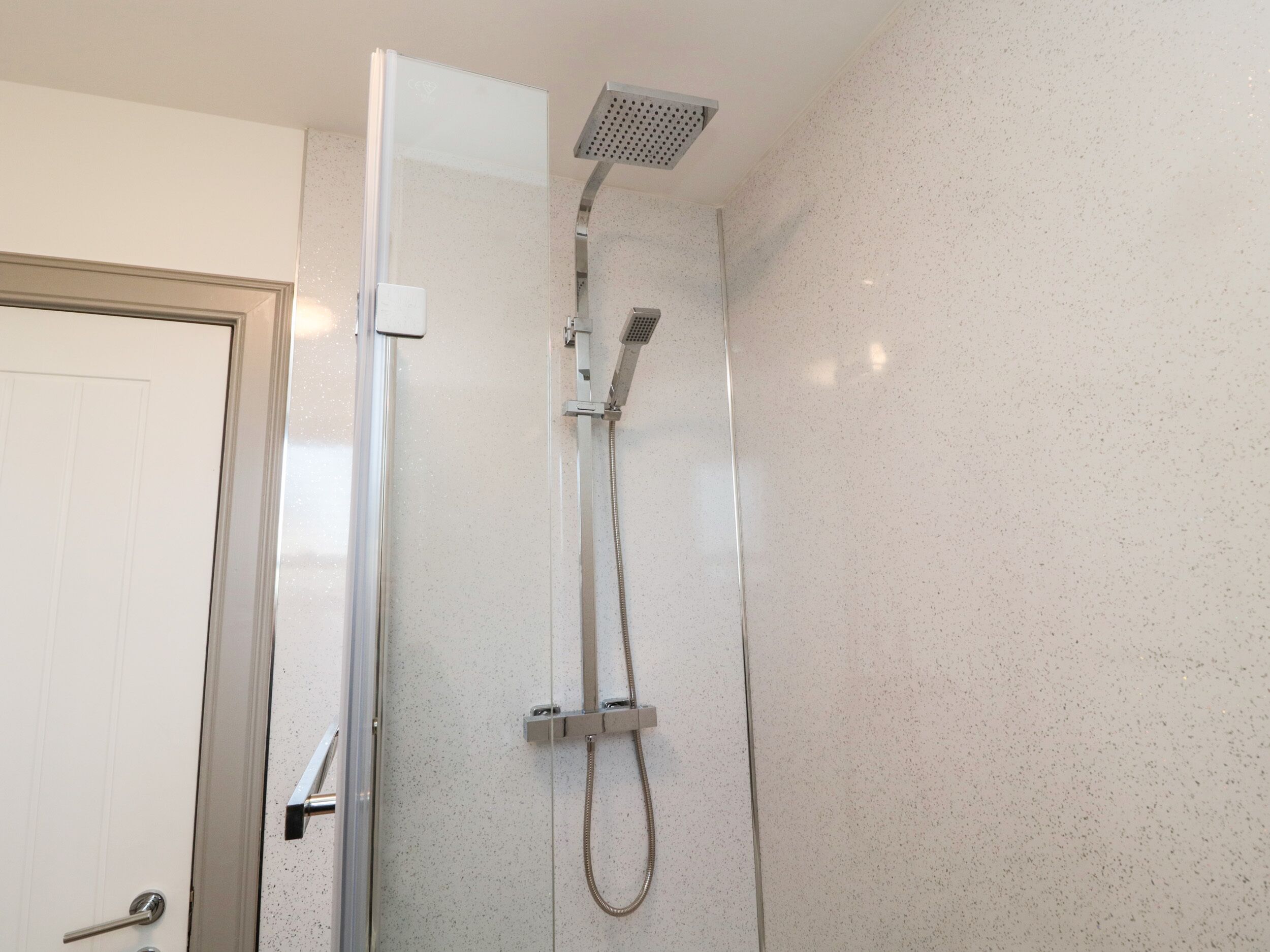 A modern bathroom with a glass shower enclosure, a handheld showerhead, and a wall-mounted faucet.