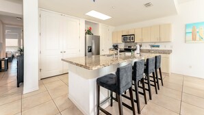 Una cocina moderna con una isla central, taburetes de bar, un refrigerador y un microondas.