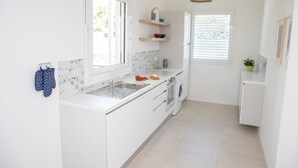 Eine moderne Küche mit weißen Schränken, einem Backofen, einer Spüle und einem Fenster mit Jalousien.
