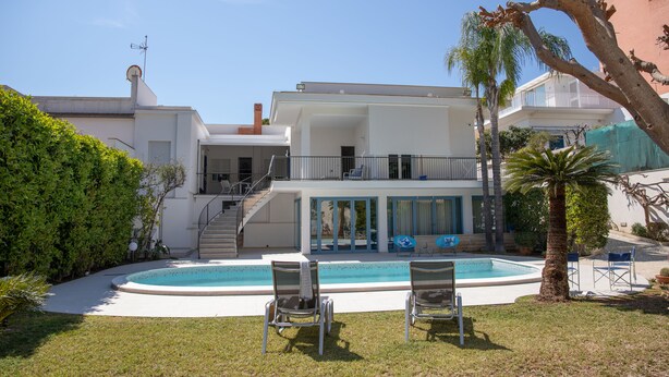 Ein zweigeschossiges Haus mit Pool, Sitzgelegenheiten im Freien und einer Treppe, die zu einem Balkon führt.