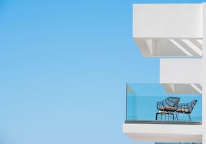 A modern building with white structural elements and a glass balcony with two chairs.