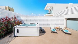 Un espace piscine extérieur moderne, doté d’un jacuzzi, de chaises longues et d’une clôture blanche.