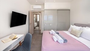 Une chambre d’hôtel avec un lit, un bureau, une chaise, une télévision et une salle de bain visible à travers une porte ouverte.