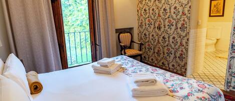 A hotel room with a bed, a chair, a bathroom, and a view of greenery outside.