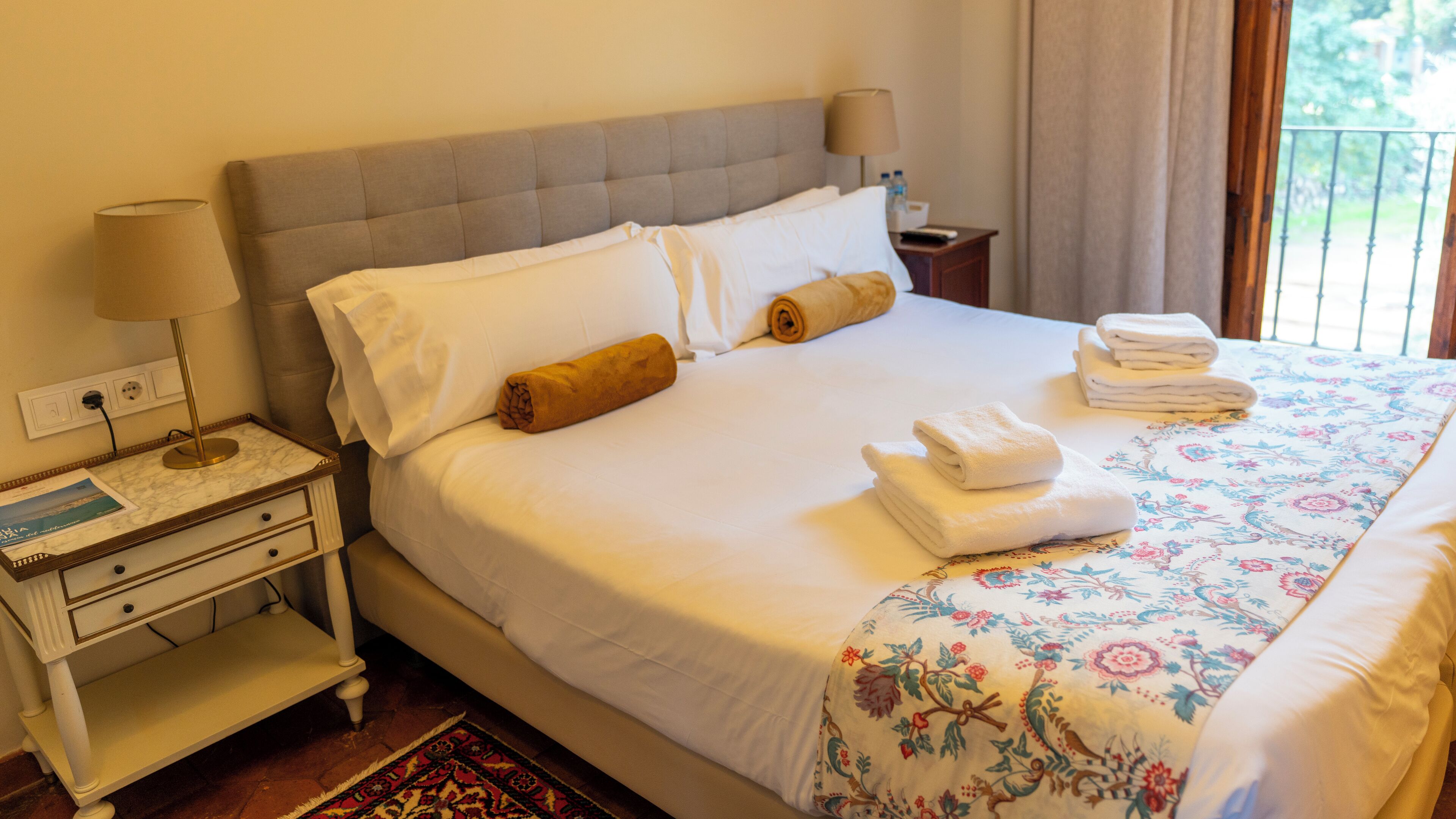 Un lit bien fait, avec des draps blancs, une couvre-lit à motifs floraux et des serviettes enroulées.