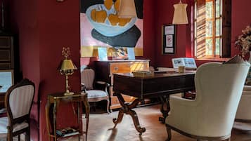A room with a desk, chairs, a lamp, a painting, and a window with a view.
