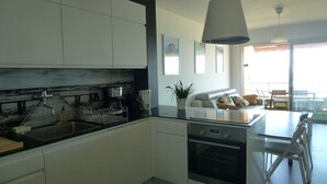 Eine moderne Küche mit weißen Schränken, einer schwarzen Arbeitsplatte und einem eingebauten Backofen. Es gibt eine Essecke mit Tisch und Stühlen, sowie einen Balkon mit Blick.