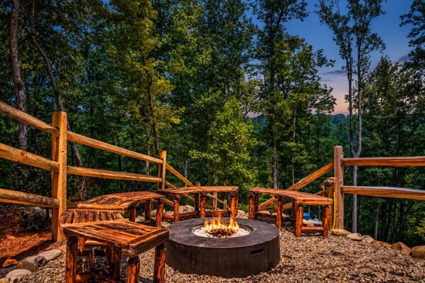 A circular fire pit surrounded by wooden benches in a forested area.