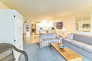 A living room with a sofa, a chair, a wooden coffee table, and a kitchen in the background.