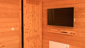 Une pièce aux murs lambrés, avec un téléviseur fixé au mur, une porte et un radiateur.