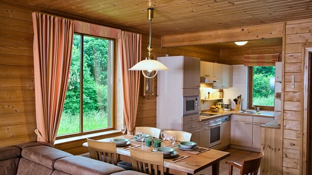 L’intérieur chaleureux d’un chalet comprend un coin repas, une cuisine et de grandes fenêtres qui offrent une vue sur la forêt.