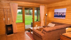 L’intérieur d’un chalet accueillant, avec un canapé, une table, une cheminée et une grande fenêtre agrémentée de rideaux.