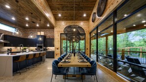 Uma cozinha moderna com uma mesa de jantar comprida e cadeiras azuis, janelas amplas e teto de madeira.
