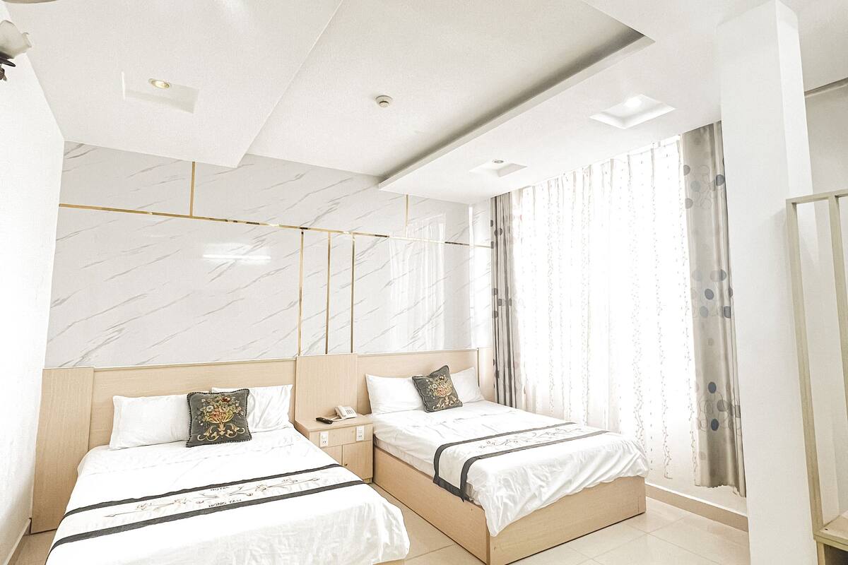 A modern hotel room with two beds, a ceiling fan, and a large window with curtains.