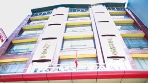 L’entrée d’un hôtel, avec une façade rouge et blanche, un escalier menant à l’entrée et une enseigne indiquant « Hôtel Hồng Tâm ».