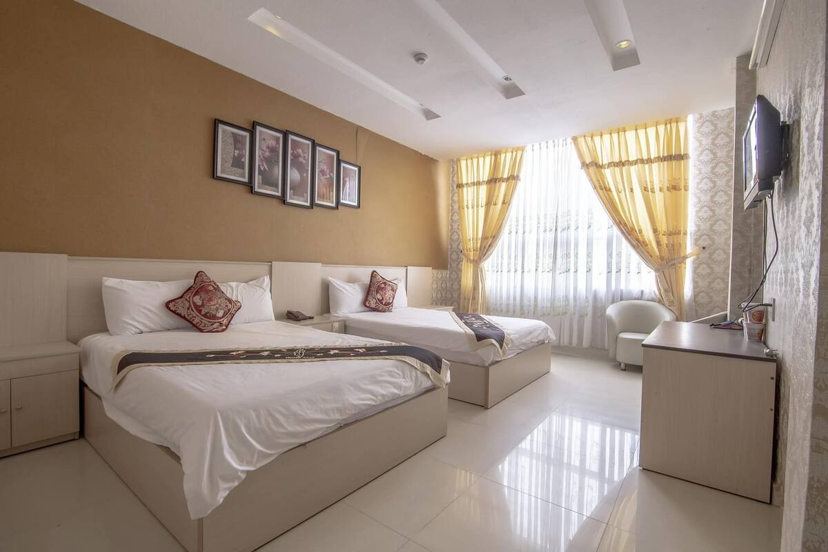 A hotel room with two beds, a desk, a chair, and a TV mounted on the wall.