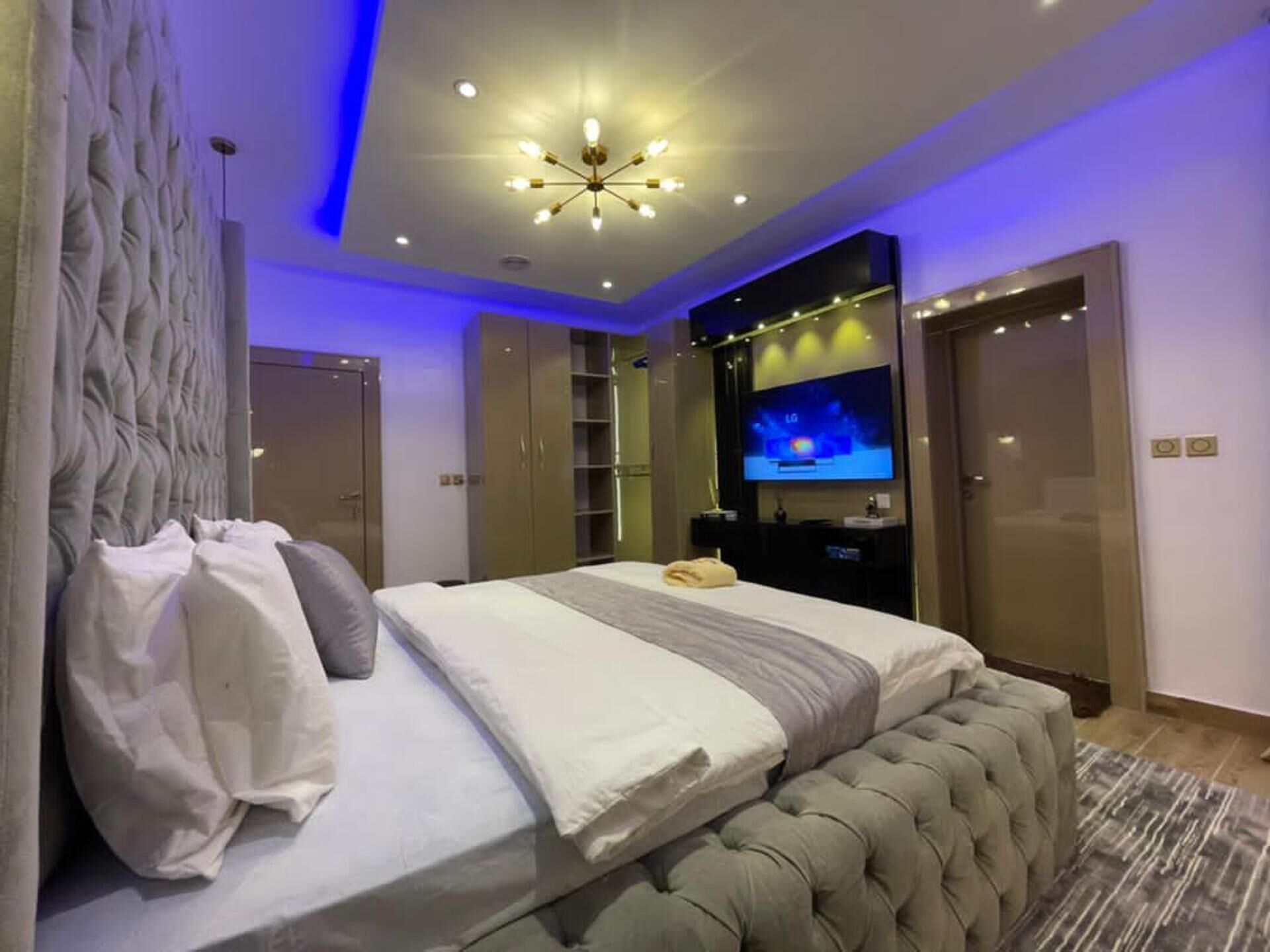 A modern bedroom with a large bed, a tufted headboard, a television, and a ceiling light fixture.