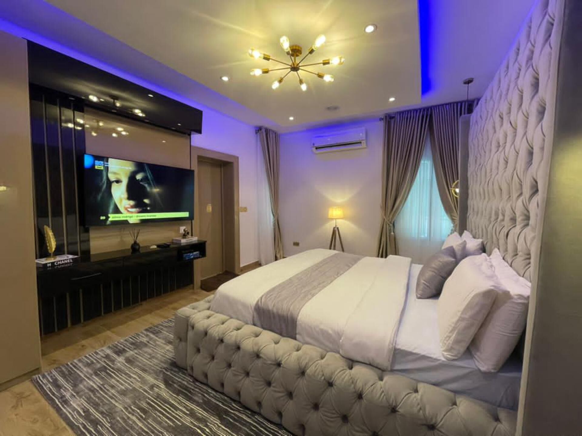 A modern bedroom with a large bed, a TV mounted on the wall, and a ceiling light fixture.