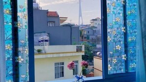 A room with a window overlooking a cityscape, a small table with a vase of flowers, and two chairs. - La Casa Homestay Ha Long (Bai Chay)