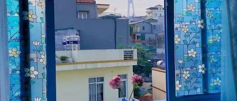 A room with a window overlooking a cityscape, a small table with a vase of flowers, and two chairs.