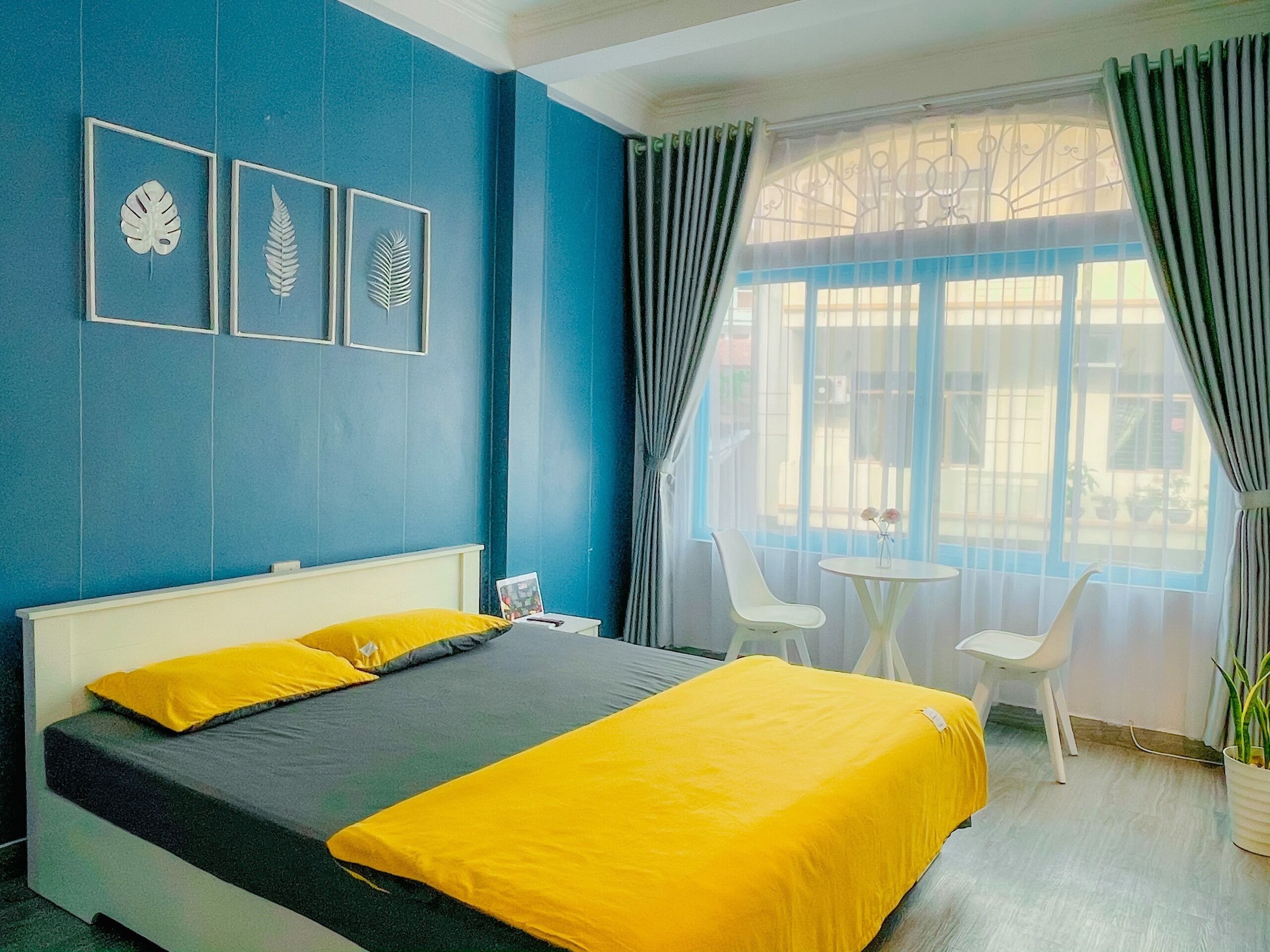 A hotel room with a bed, a small table with chairs, and a window with curtains.