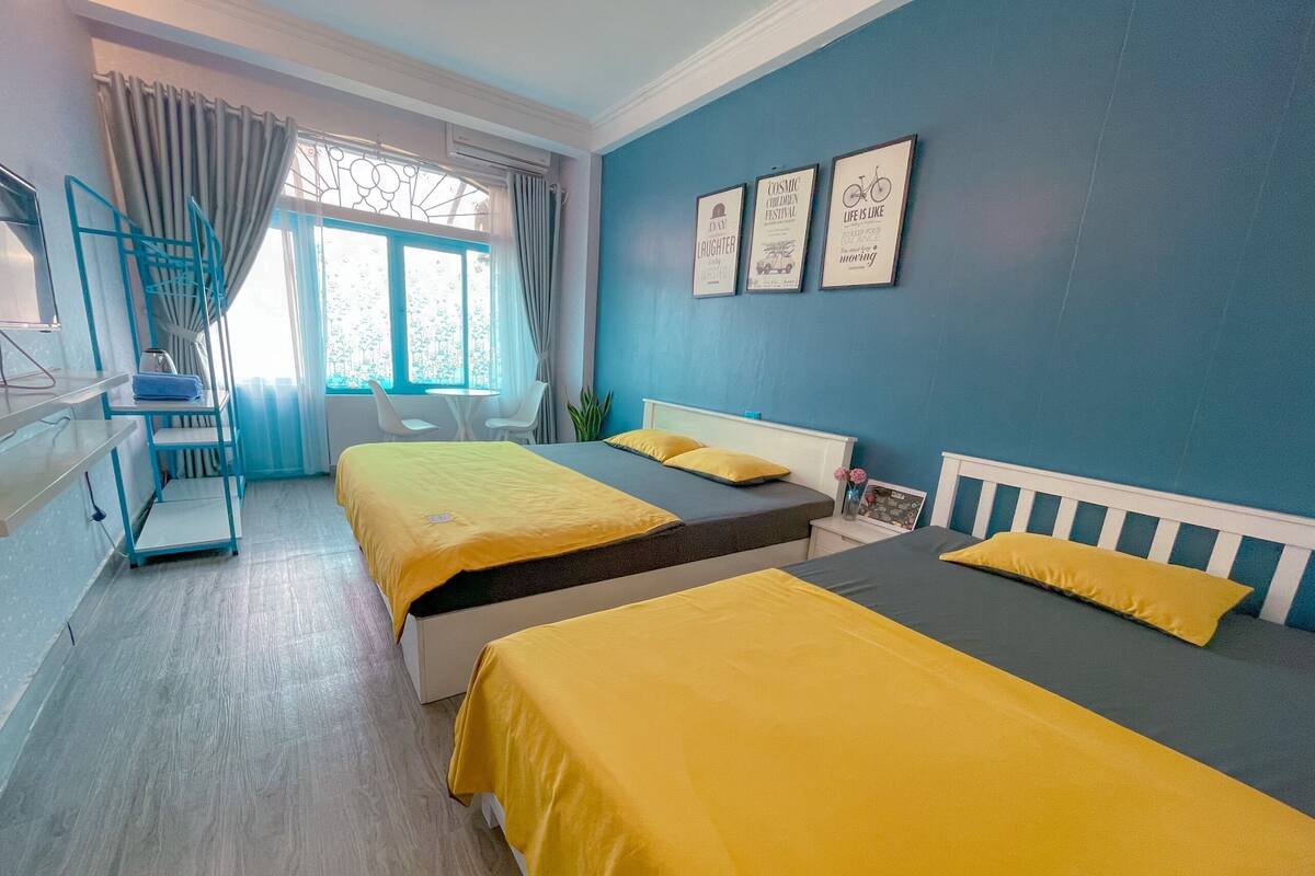A hotel room with two beds, a desk, a chair, and a window with curtains.
