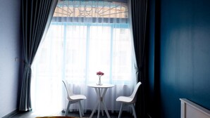 A room with a round table and two chairs, a window with sheer curtains, and a blue wall. - La Casa Homestay Ha Long (Bai Chay)