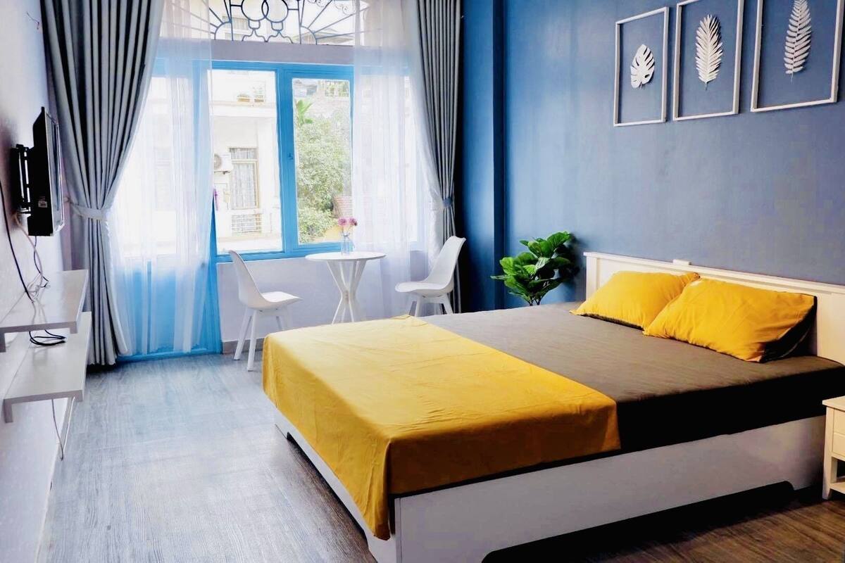 A bedroom with a bed, two chairs, a small table, and a plant.