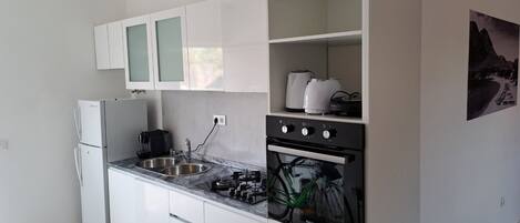 Una cocina con armarios blancos, un lavamanos doble, una estufa y una cafetera.