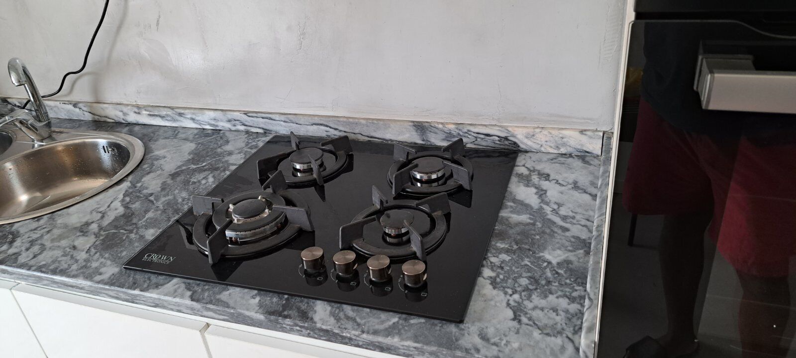 Una cocina con estufa a gas de cuatro quemadores, un lavamanos de acero inoxidable y encimera de mármol.