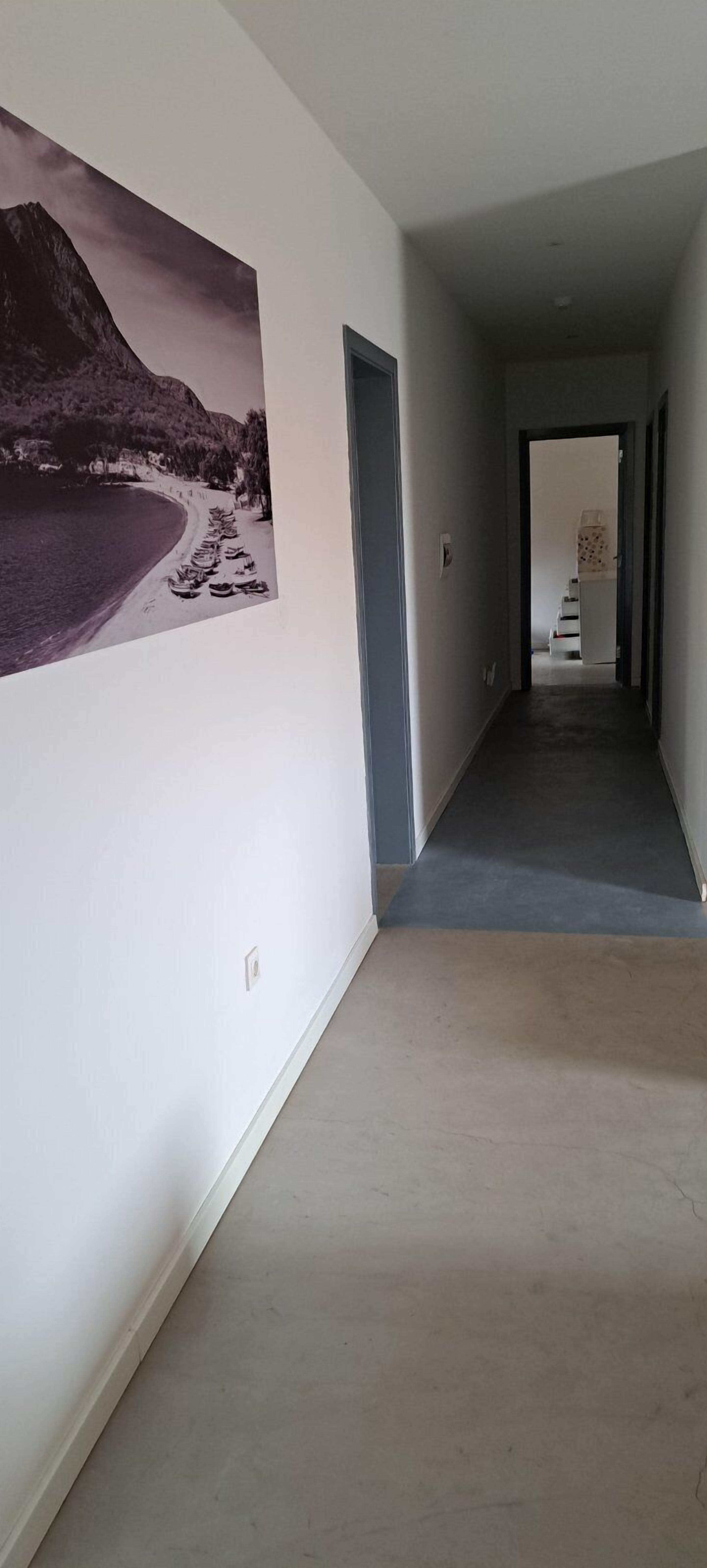 A hallway with a large beach photograph on the wall, a door on the right, and a staircase in the background.