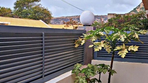Een klein balkon met een metalen stoel, een plant in pot en een witte muur.