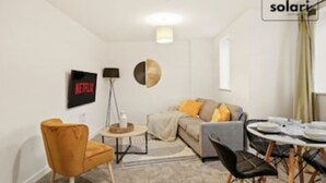 En moderne stue med sofa, lænestole, sofabord og fjernsyn hængt på væggen.
