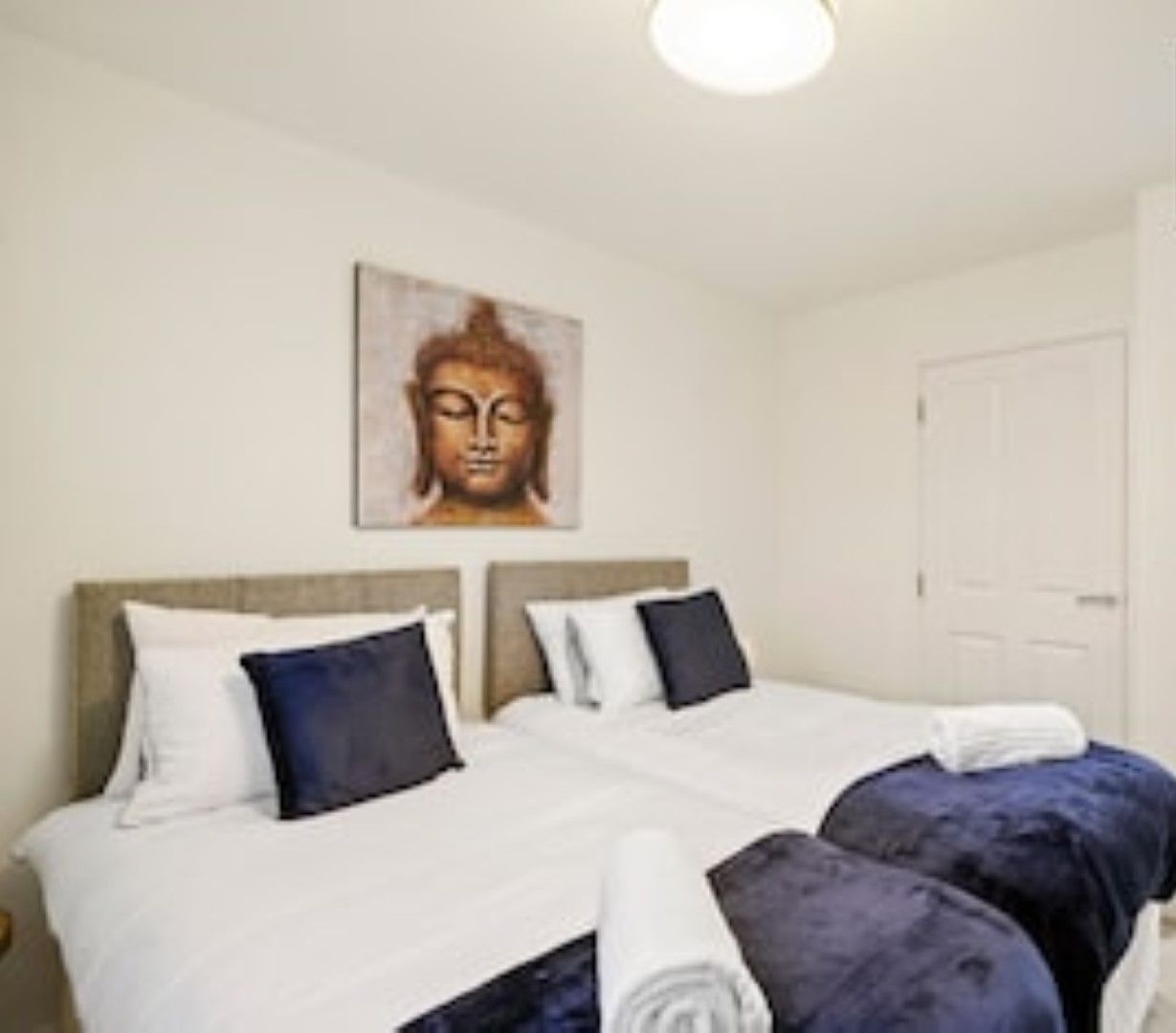 A hotel room with a bed, a wall-mounted Buddha statue, and a door.