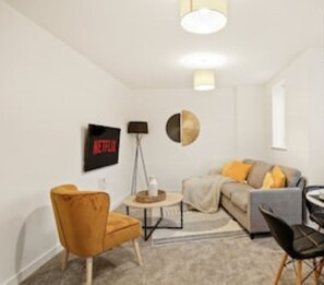 A modern living room with a sofa, armchairs, a coffee table, and a TV mounted on the wall. - Peterborough Serviced Accommodation - Lux 2 Bed Apartment | Solari Living (Peterborough)