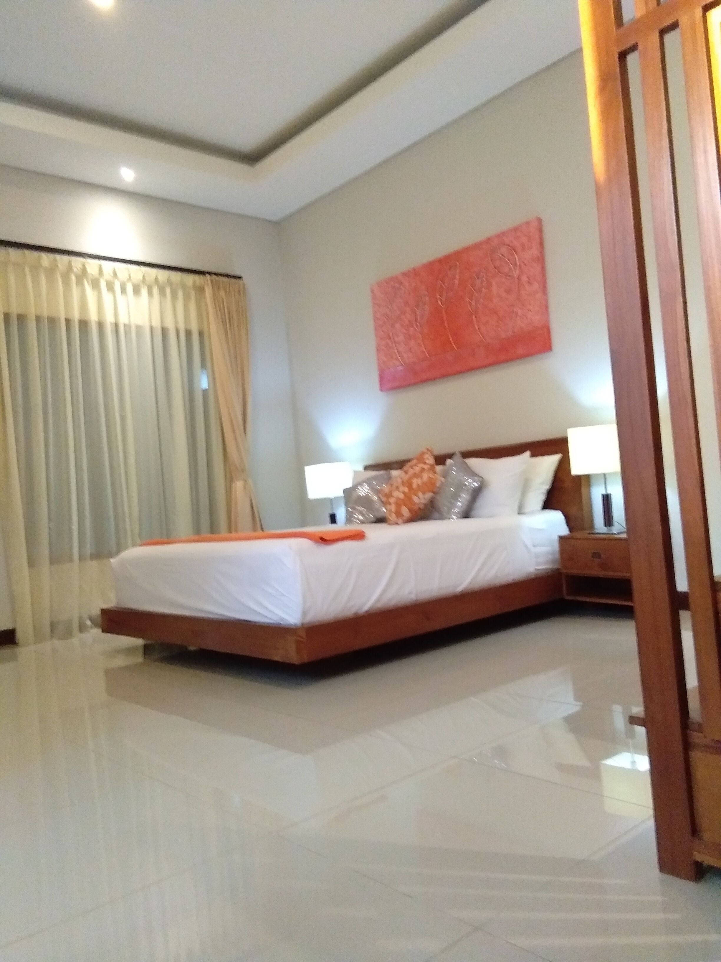 A modern hotel room with a large bed, a nightstand, a wall-mounted lamp, and a window with curtains.