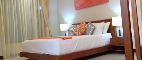 A modern hotel room with a large bed, a nightstand, a wall-mounted lamp, and a window with curtains.
