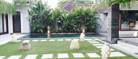 Un patio con piscina, faroles de piedra y abundante vegetación.
