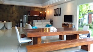 A spacious living area with a large wooden dining table, white sofas, and a TV. - Gathering With 5 Bedroom Center House Villa (Legian)