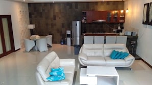 A modern living room with two white sofas, a coffee table, and a dining area with a kitchen in the background. - Gathering With 5 Bedroom Center House Villa (Legian)